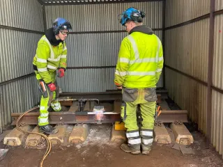 To deltakere følger arbeidet med utstyr ved en skinneskjøt